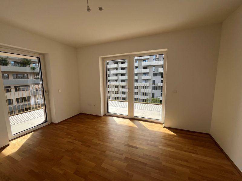 Helles Zimmer mit Parkettboden und großen Fenstern, die Zugang zu einem Balkon bieten und Stadtblick ermöglichen.