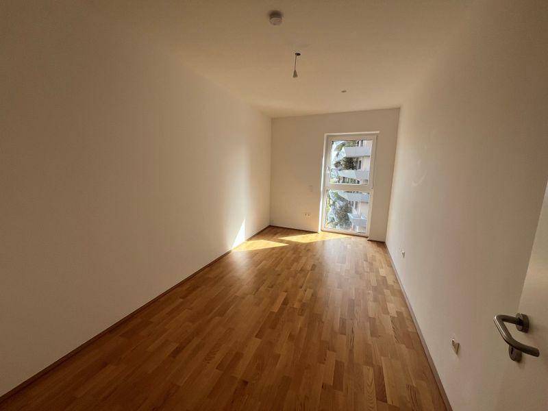 Helles Zimmer mit Parkettboden und einem Fenster, das viel Tageslicht hereinlässt.