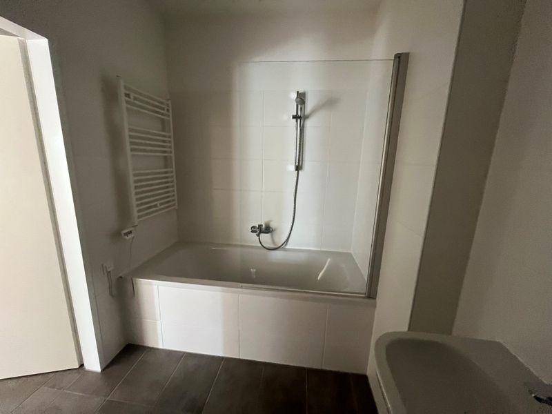 Badezimmer mit Badewanne, Duschfunktion, beheiztem Handtuchhalter und Waschbecken.