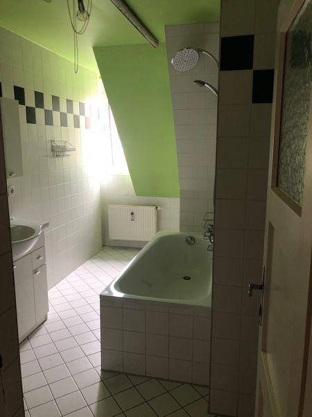 Badezimmer mit Badewanne, Dusche und Dachschräge, hell gefliest mit grüner Decke.