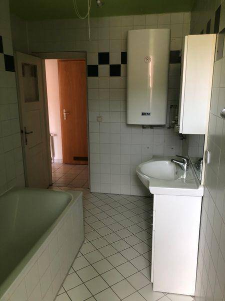 Badezimmer mit Badewanne, Waschbecken und Boiler, hell gefliest mit grüner Decke.