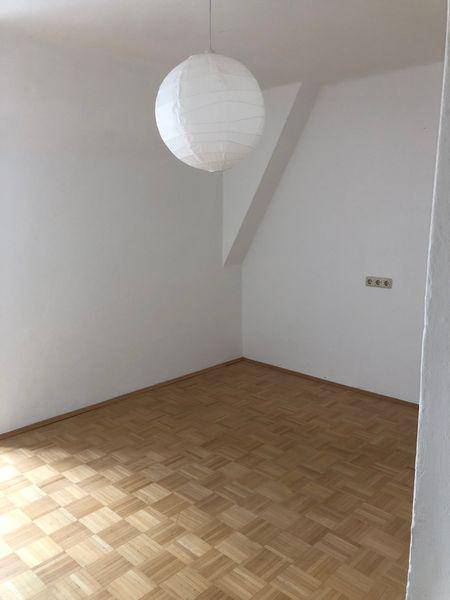 Leeres Zimmer mit Parkettboden, weiß gestrichenen Wänden und einfacher Deckenleuchte.
