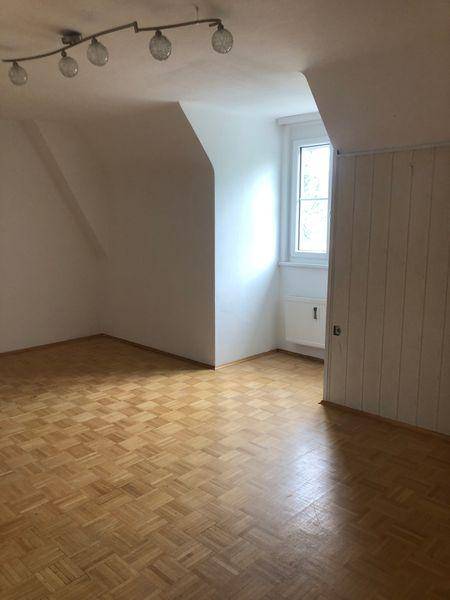 Leeres Zimmer im Dachgeschoss mit Parkettboden, Dachschräge und Fenster.