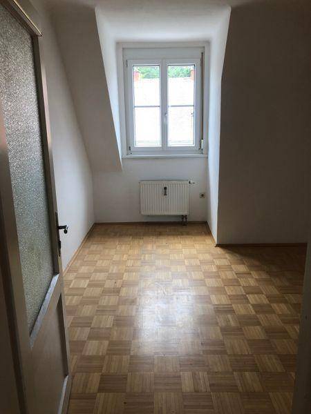Helles Zimmer im Dachgeschoss mit Parkettboden, Dachschräge und Fenster.