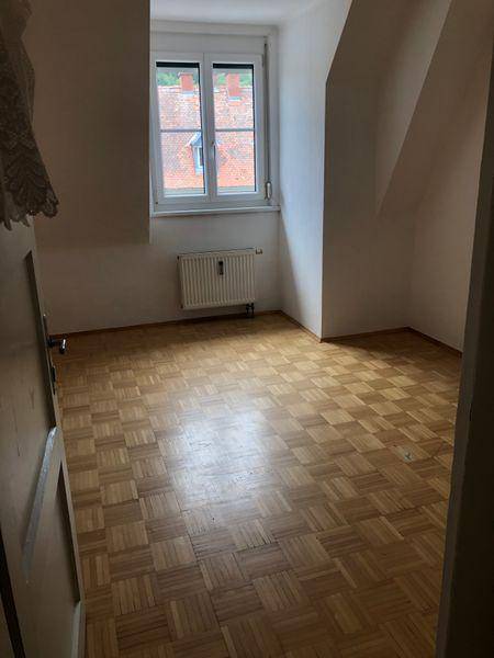 Helles Zimmer im Dachgeschoss mit Parkettboden, Dachschräge und Blick nach draußen.