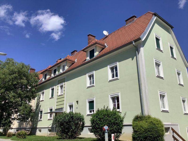 Mehrfamilienhaus mit hellgrüner Fassade und Satteldach unter blauem Himmel.