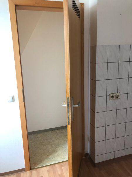 Küchenbereich mit Laminatboden und weißen Wandfliesen, Zugang zu einem weiteren Raum.
