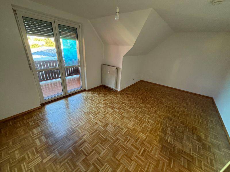 Helles Schlafzimmer mit Parkettboden, Dachschräge und Zugang zu einem Balkon.