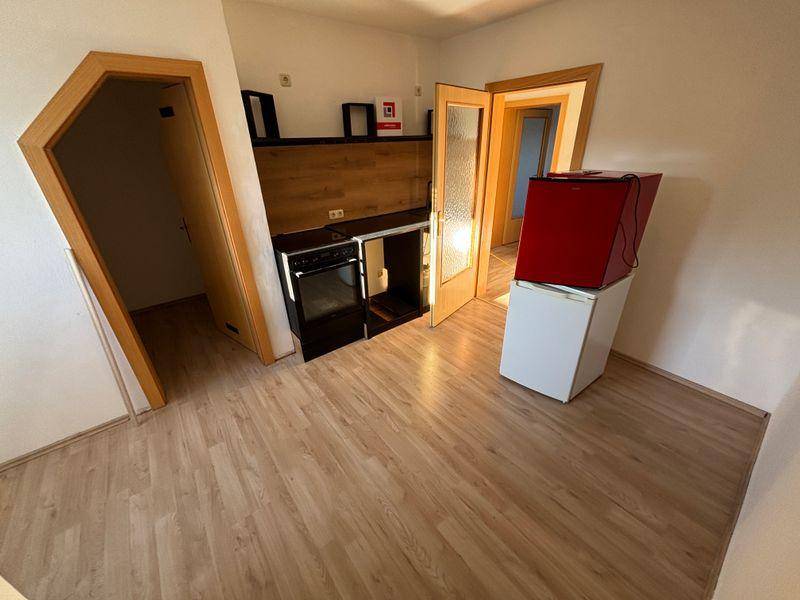 Kleine Küchenzeile mit Kochfeld und Ofen, integriert in einen Wohnbereich mit Laminatboden.