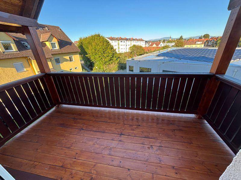 Sonniger Balkon mit Holzboden und Brüstung, bietet einen weiten Blick über die Umgebung.