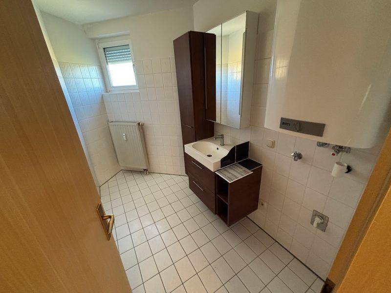 Badezimmer mit Fliesenboden, Waschbecken, Spiegelschrank und Fenster für Tageslicht.
