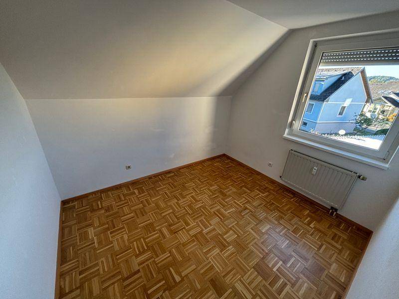 Helles Zimmer mit Parkettboden und Dachschräge, bietet einen Ausblick auf die Nachbarschaft.
