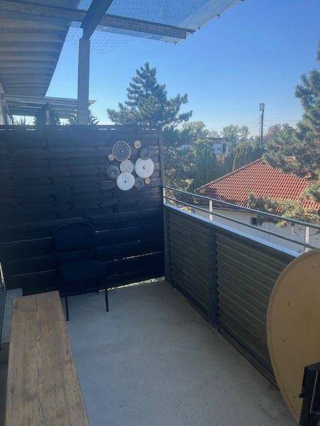 Überdachter Balkon mit Holzwand, Sitzgelegenheit und weitem Blick ins Grüne.