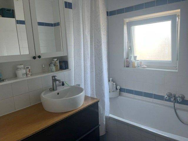 Badezimmer mit modernem Aufsatzwaschbecken, Holzplatte und Spiegelschrank über der Badewanne.