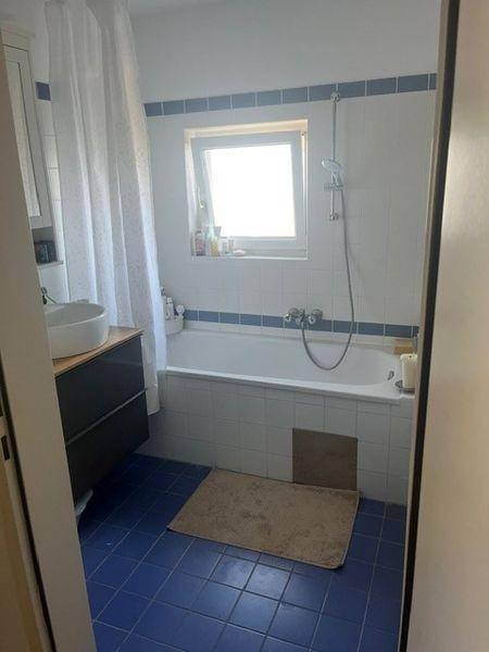 Badezimmer mit Badewanne, blauen Fliesen und Fenster für natürliches Tageslicht.