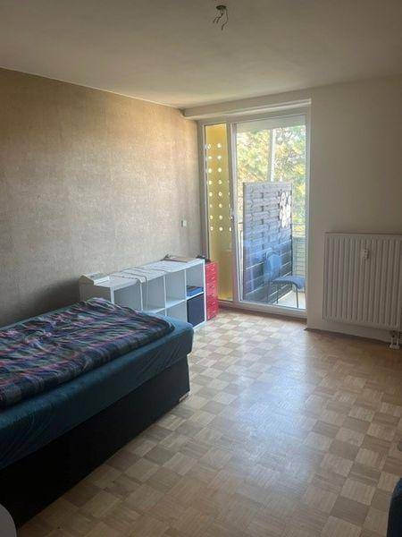 Helles Schlafzimmer mit Einzelbett, Laminatboden und direktem Zugang zum Balkon.