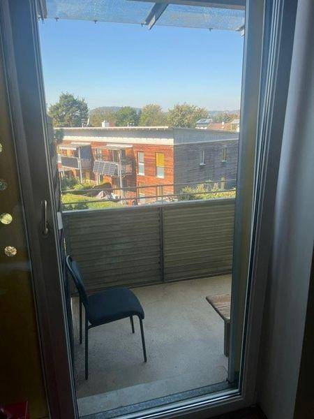 Balkon mit Sitzgelegenheit und Blick auf die umliegenden Gebäude und grüne Umgebung.