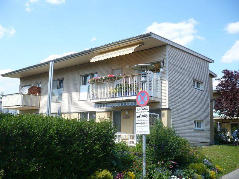 Modernes Mehrfamilienhaus mit Holzfassade, Balkonen und gepflegtem Vorgartenbereich.