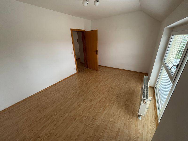 Helles Zimmer im Dachgeschoss mit Laminatboden, Dachschräge und Fenster mit Heizkörper.
