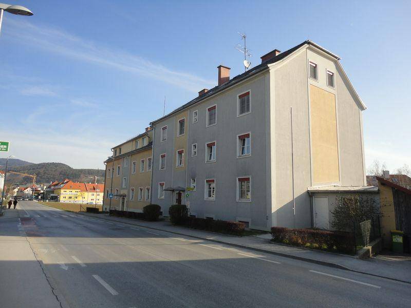 Mehrfamilienhaus mit mehreren Etagen und Satteldach an einer Straße gelegen.