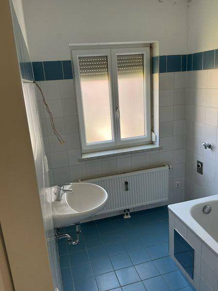 Badezimmer im Stil der 80er Jahre mit blauen und weißen Fliesen, Waschbecken und Badewanne.