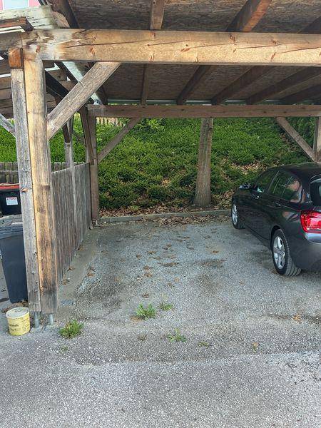 Holz-Carport mit Stellplatz für ein Fahrzeug und Mülltonnen im Vordergrund.