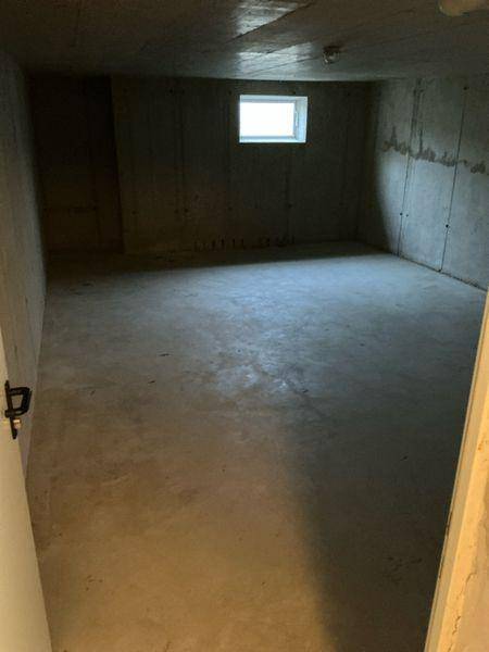 Unfertiger Kellerraum mit Betonwänden und kleinem Fenster, ideal als Lagerfläche.