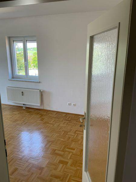 Heller Raum mit Parkettboden und Fenster, das einen weiten Blick ins Grüne bietet.