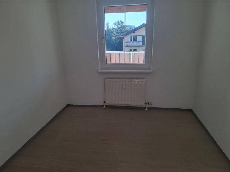 Helles Zimmer mit Fenster und Heizkörper, ausgestattet mit modernem Laminatboden.