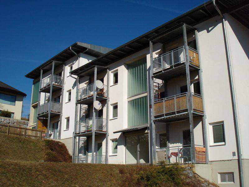 Ansicht eines modernen Wohngebäudes mit mehreren Balkonen und einer hellen Fassade unter klarem blauem Himmel.
