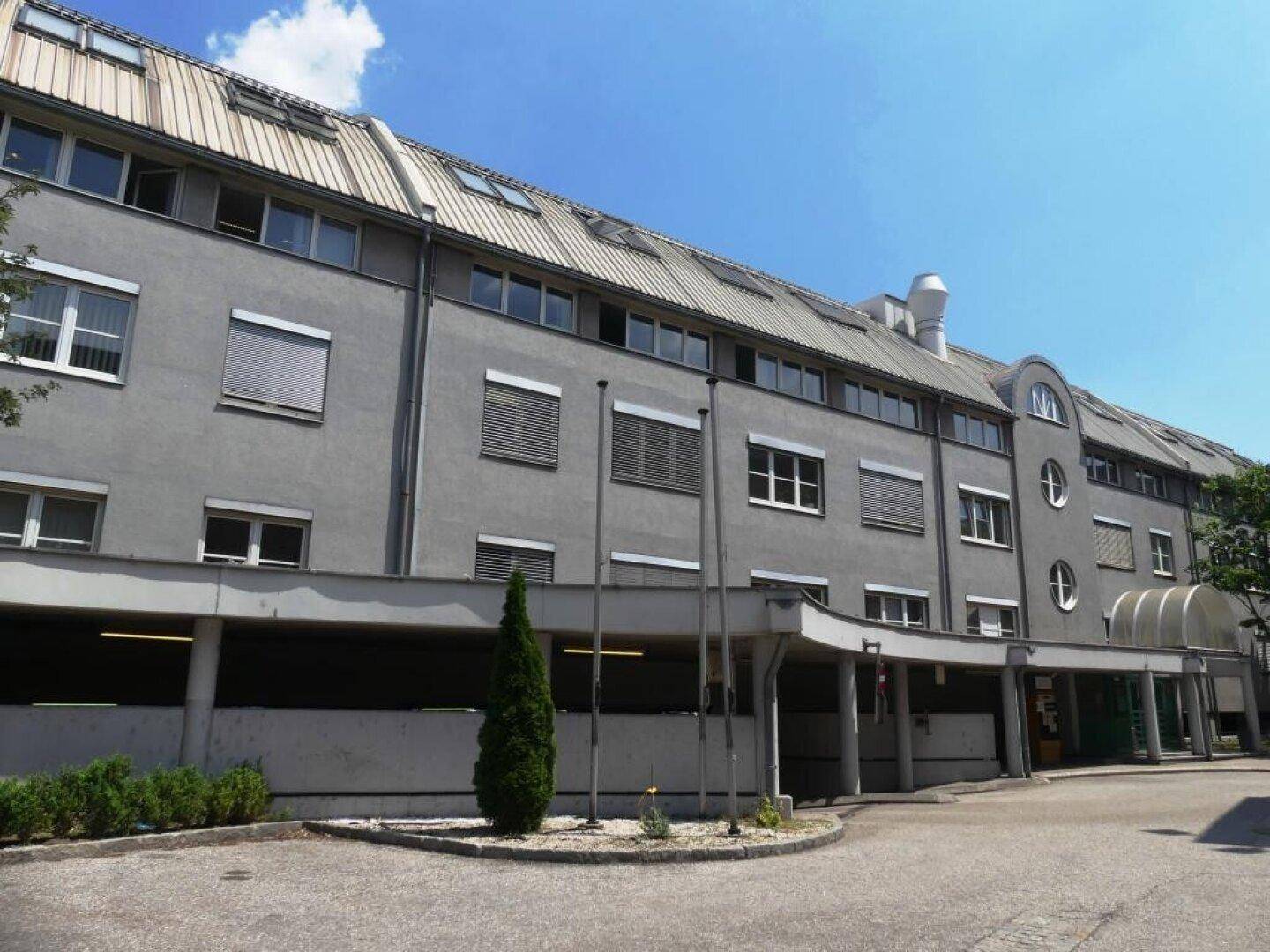 Mehrstöckiges Bürogebäude mit grauer Fassade, vielen Fenstern und einem überdachten Eingangsbereich.