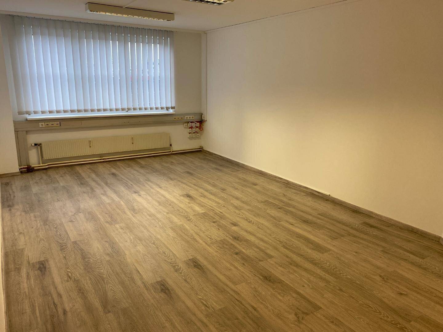 Heller und geräumiger Büroraum mit Laminatboden und Fensterfront, ideal für Arbeitsplätze.