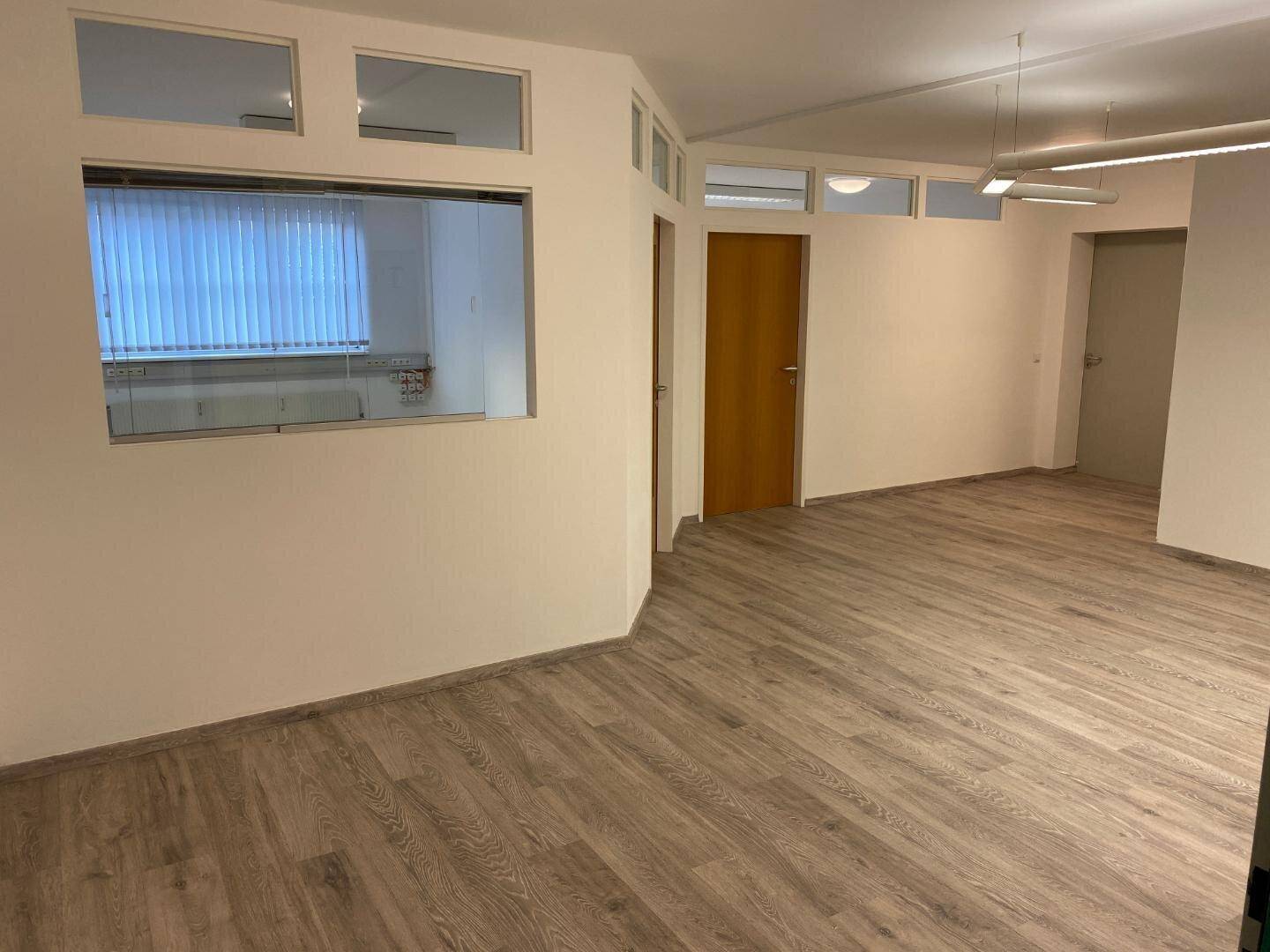 Heller, leerer Büroraum mit Laminatboden und Fenstern, bereit für neue Mieter.