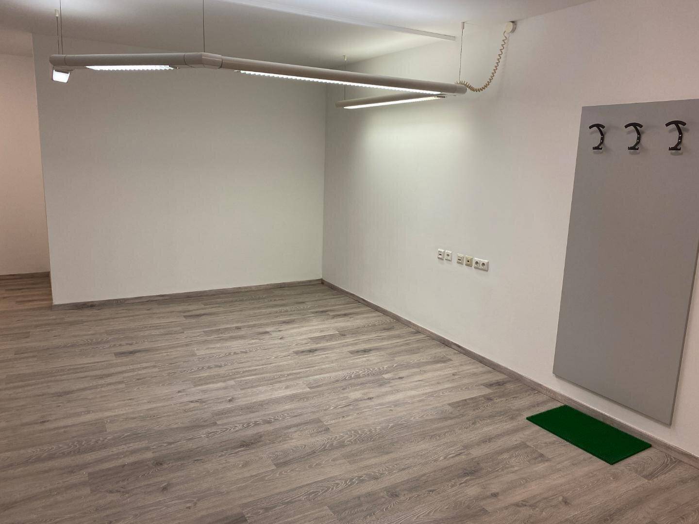 Leerer Büroraum mit Laminatboden, weißen Wänden und moderner Deckenbeleuchtung.