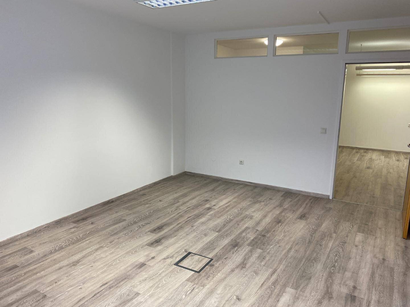 Heller Büroraum mit Laminatboden und Zugang zu einem weiteren Bereich, ideal für Bürogemeinschaften.