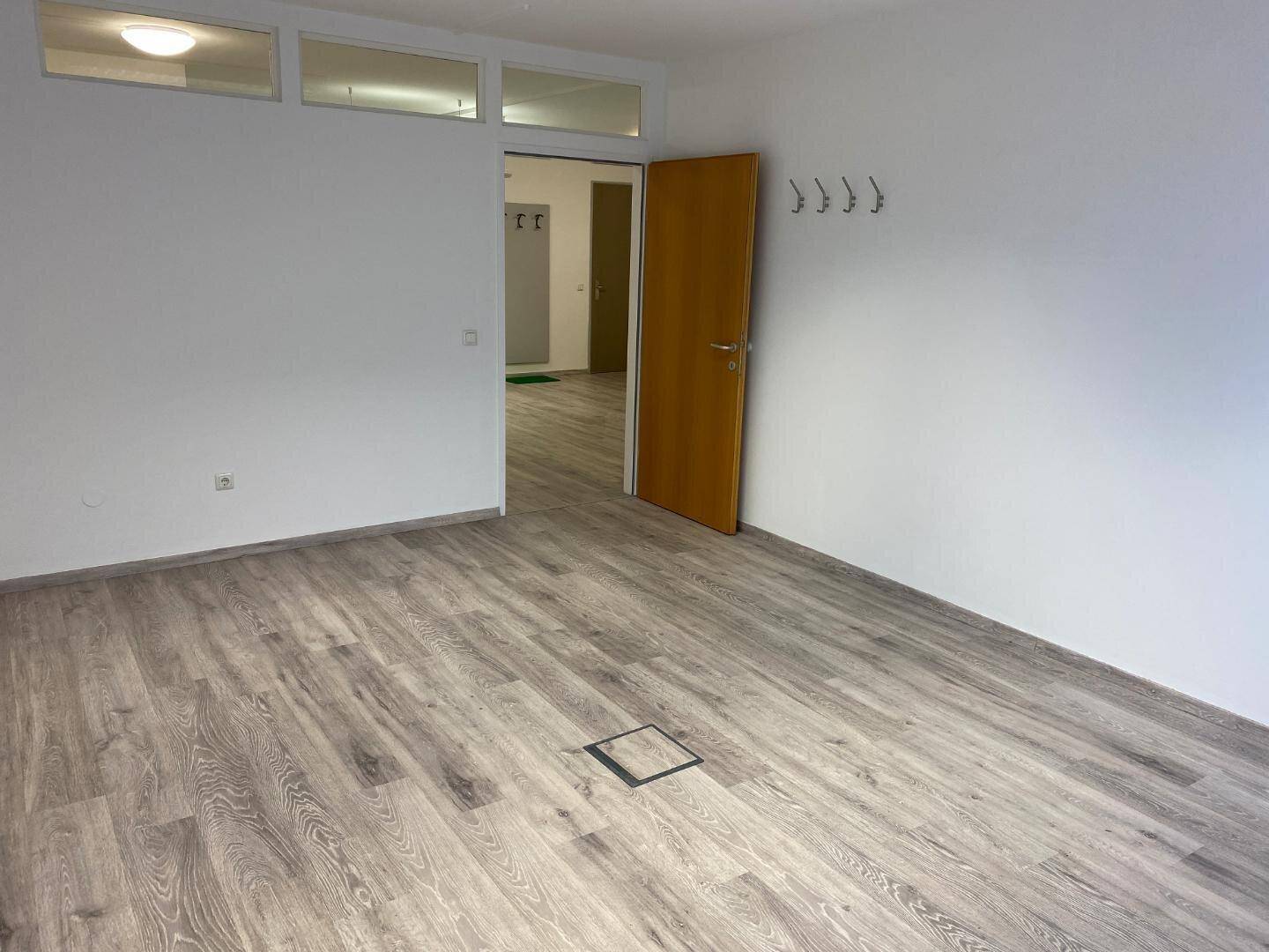 Geräumiger Büroraum mit Laminatboden, weißen Wänden und Garderobenhaken an der Wand.