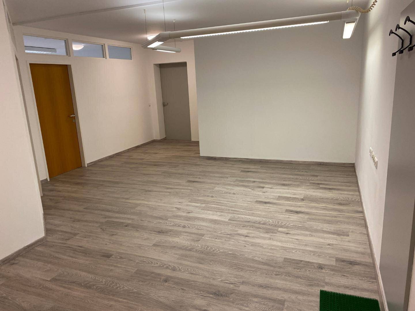 Leerer Büroraum mit hellem Laminatboden und weißen Wänden, bereit zur individuellen Gestaltung.