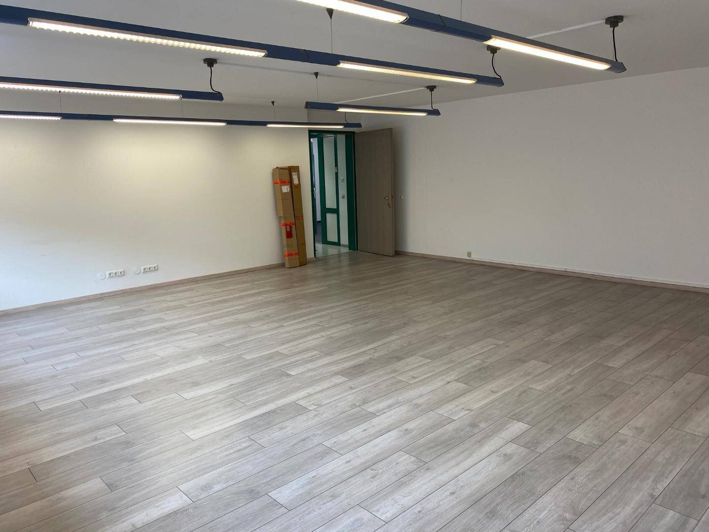 Geräumiger, unmöblierter Büroraum mit hellem Boden, weißen Wänden und einer Tür im Hintergrund.