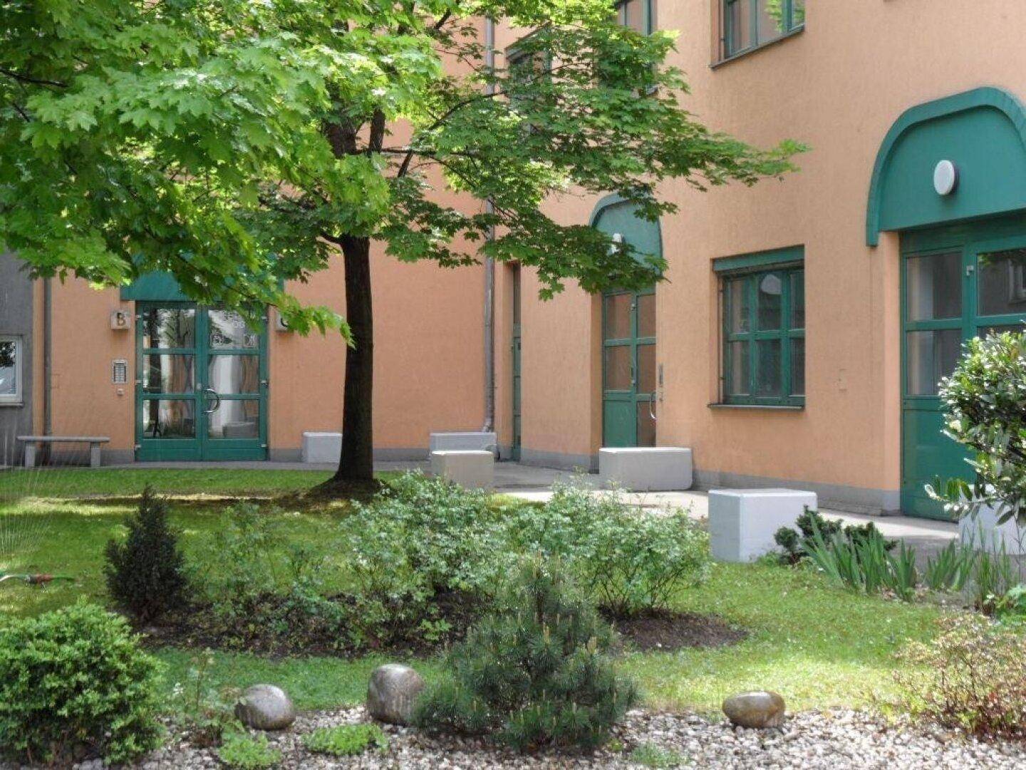 Gepflegter kleiner Gartenbereich mit Bäumen, Sträuchern und einem Kiesweg innerhalb eines Gebäudekomplexes.