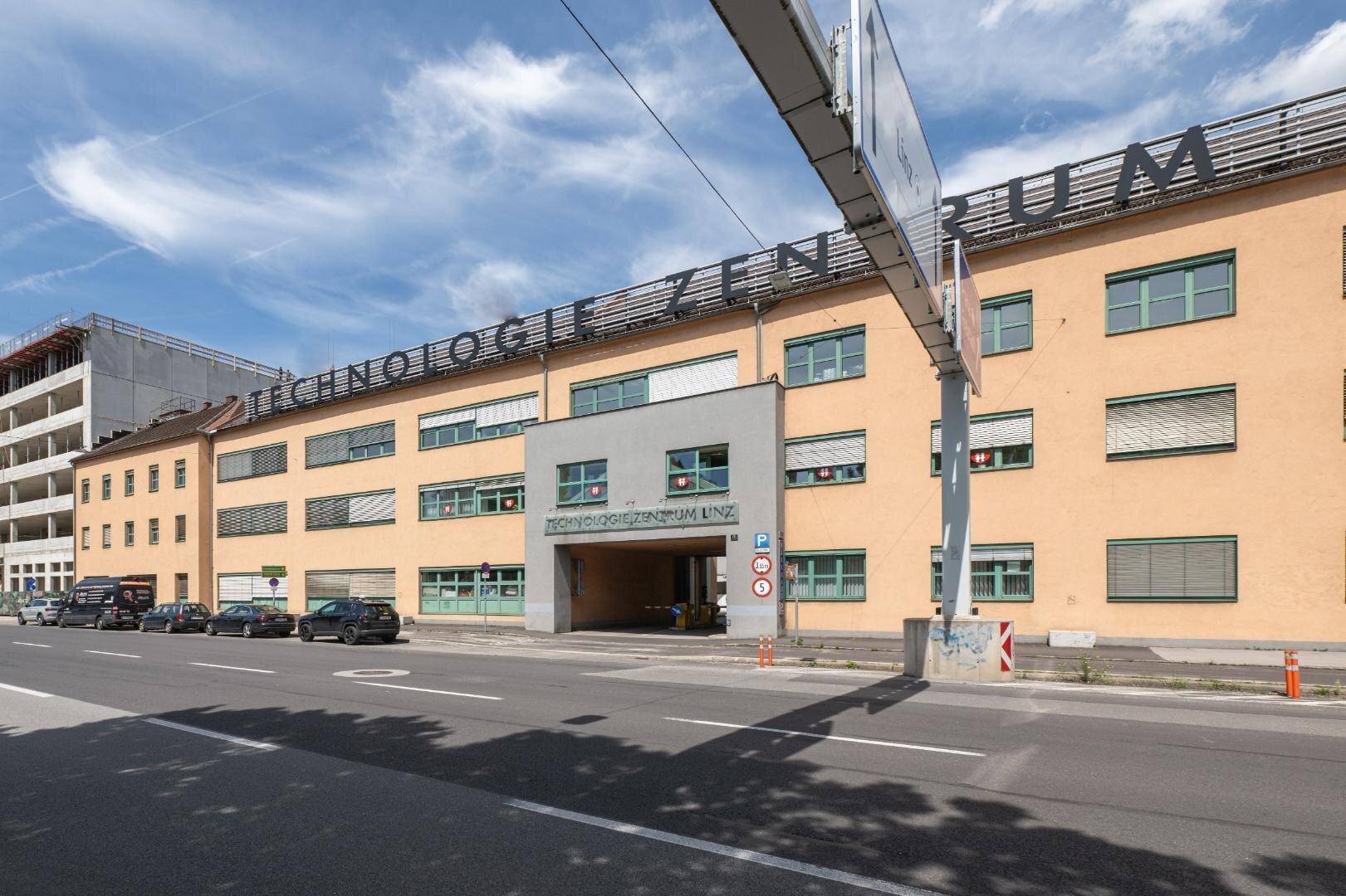 Außenansicht des Technologie Zentrums Linz von der Straße aus mit Gebäudefassade und Parkplätzen.