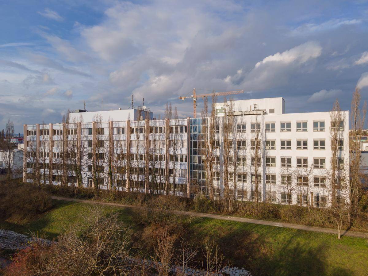Großes Bürogebäude mit moderner Fassade und vielen Fenstern, umgeben von Bäumen und Grünflächen.