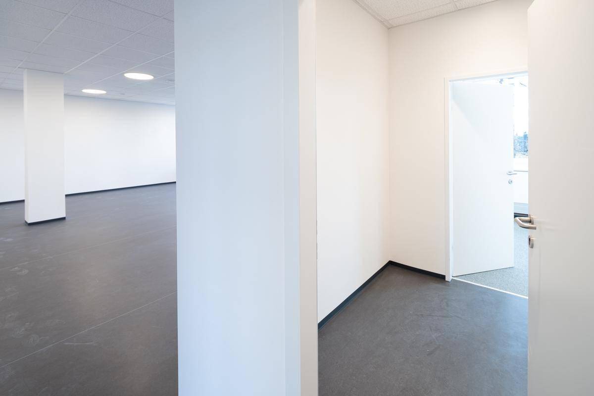 Geräumiger Flur mit dunklem Boden und Blick in angrenzende Büroräume, gekennzeichnet durch schlichte weiße Wände.