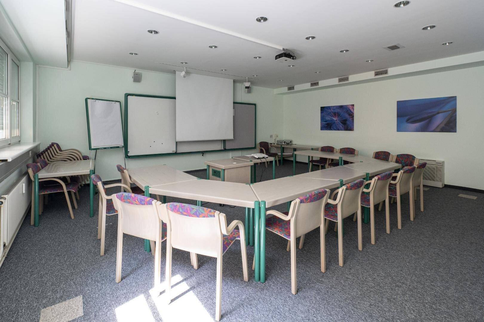 Geräumiger Konferenzraum mit U-förmiger Tischordnung, Projektor und Whiteboards für Präsentationen und Schulungen.