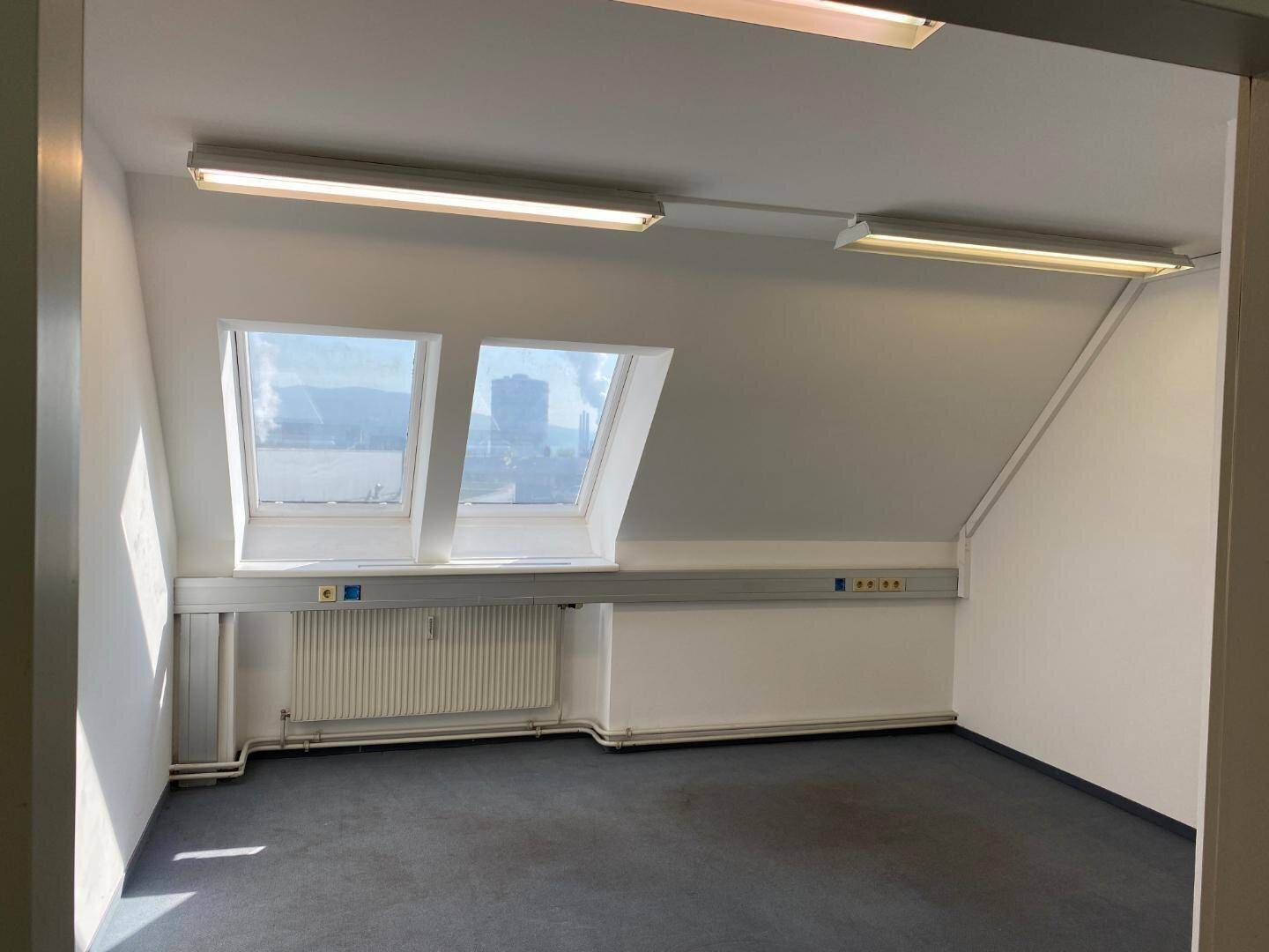 Geräumiger Büroraum im Dachgeschoss mit zwei großen Dachfenstern, Teppichboden und Heizung.
