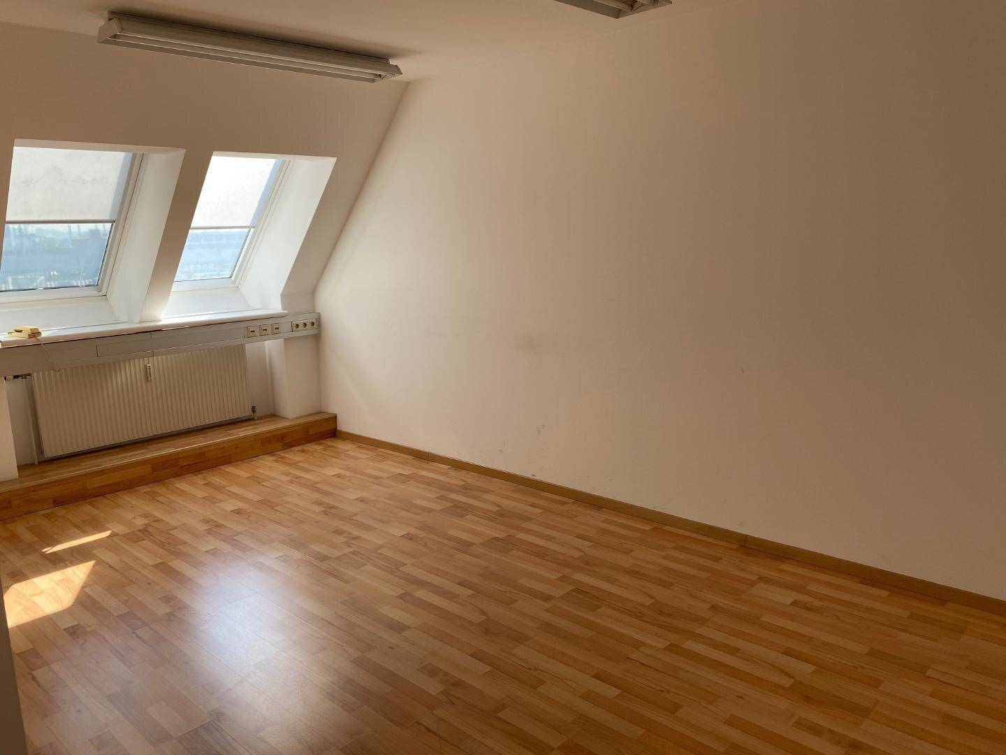 Heller Büroraum im Dachgeschoss mit Laminatboden, weißen Wänden und zwei großen Dachfenstern.