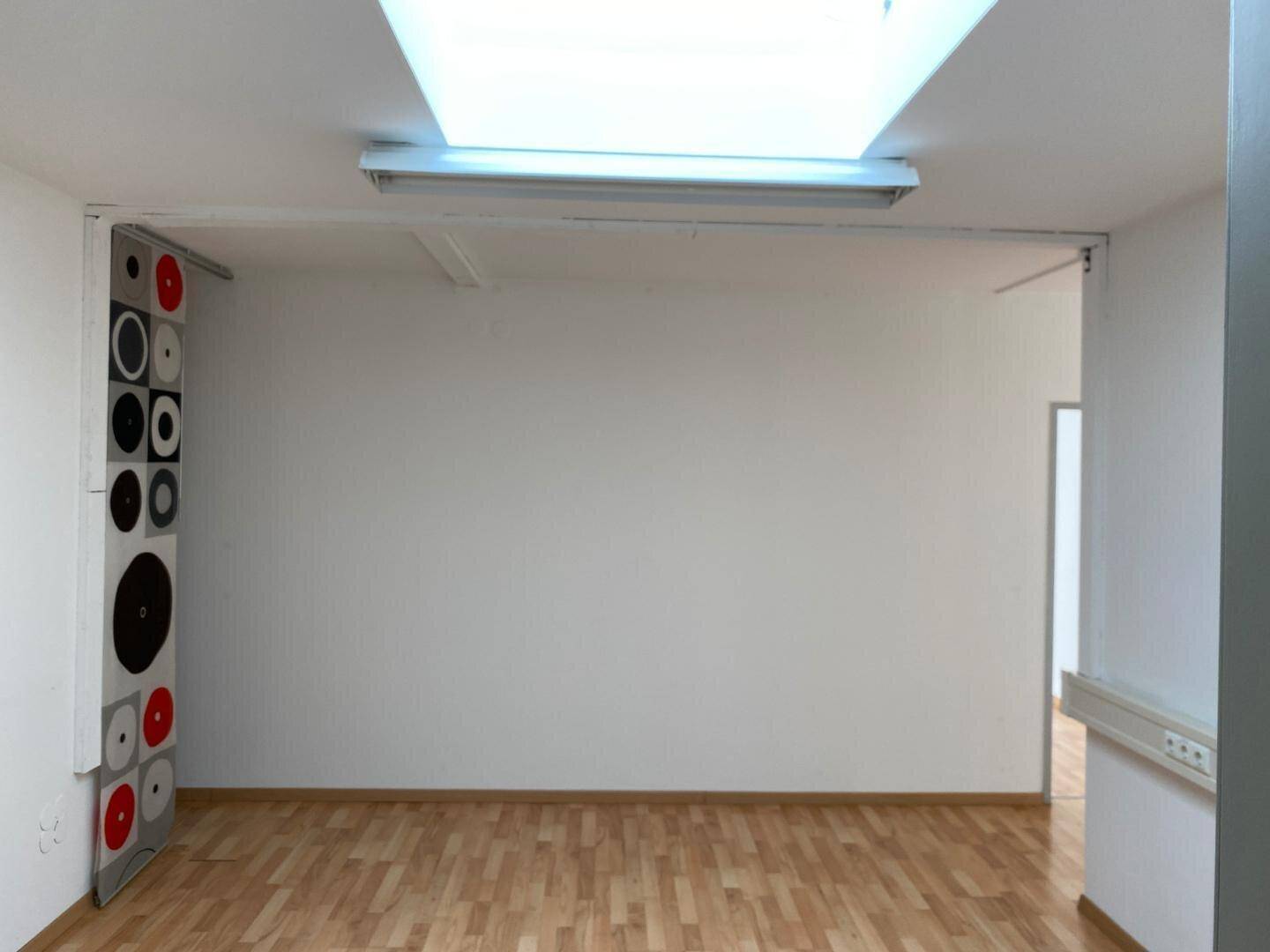 Leerer Büroraum mit hellem Laminatboden, weißen Wänden und einer dekorativen Wandverkleidung.