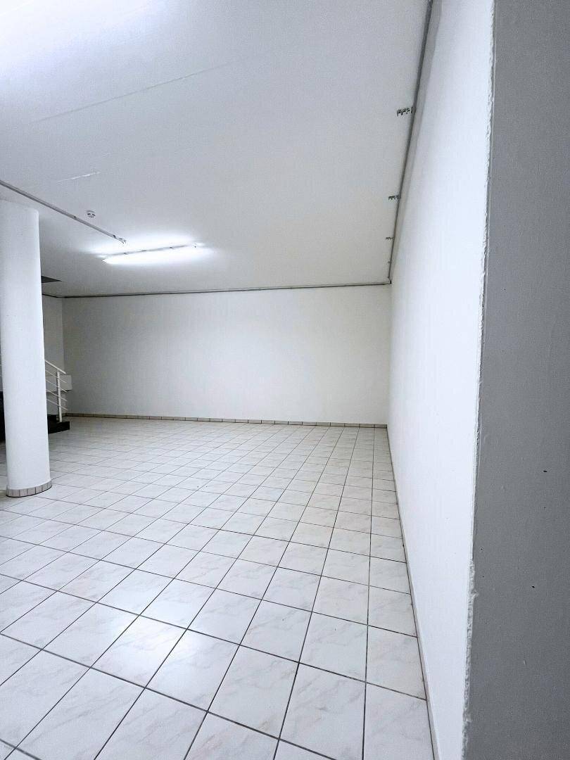 Heller, leerer Raum mit weißen Fliesenboden und schlichten weißen Wänden, ideal für gewerbliche Nutzung.