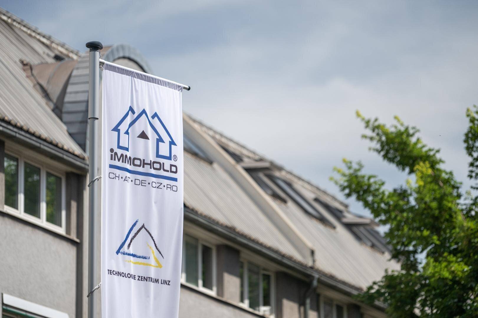 Flagge mit den Logos von IMMOHOLD und Technologie Zentrum Linz vor einem Gebäude.
