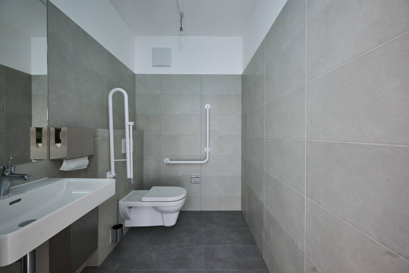 Barrierefreies Badezimmer mit Haltegriffen, wandhängendem WC und modernem Waschbecken.