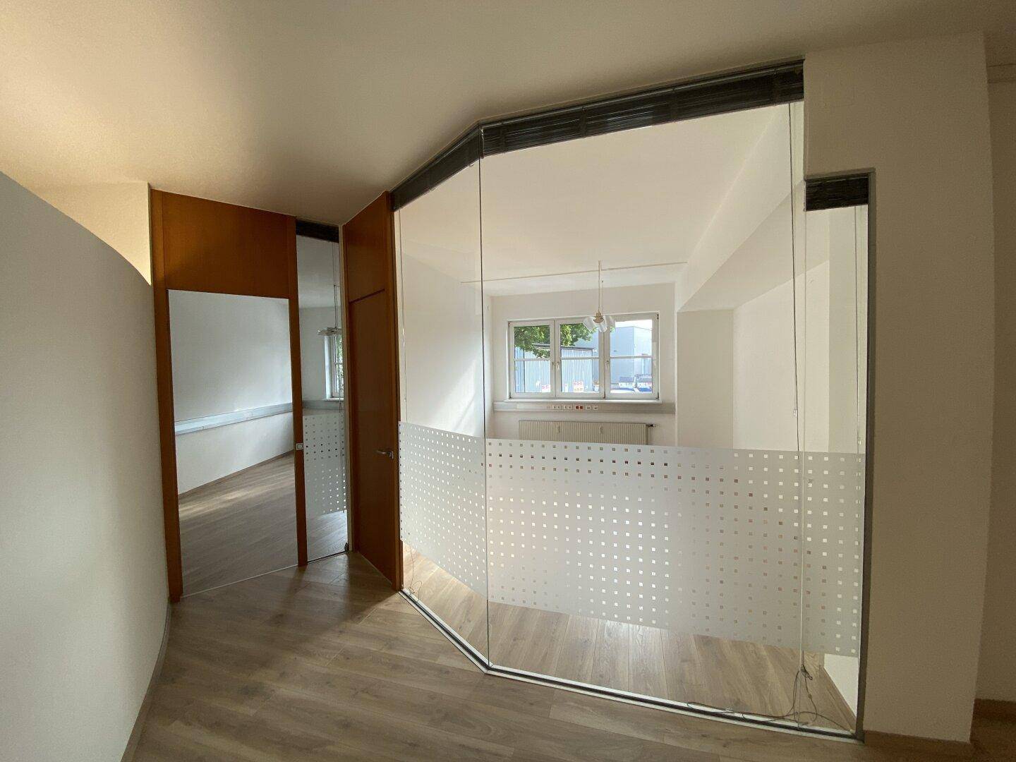 Moderner Bürobereich mit Glaswänden, die einen weiteren Raum mit Fenstern und Tageslicht reflektieren.